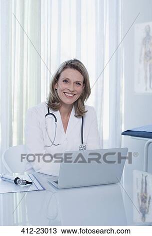 Portrait of smiling female doctor sitting at desk with laptop View Large Photo Image Stock Image - Portrait of smiling female doctor sitting at desk with laptop. Fotosearch