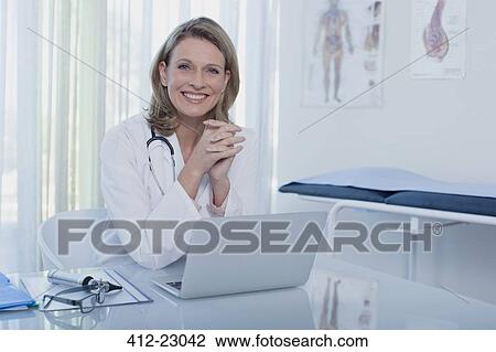 Portrait of smiling female doctor sitting at desk with laptop in office View Large Photo Image Stock Image - Portrait of smiling female doctor sitting at desk with laptop in office. Fotosearch