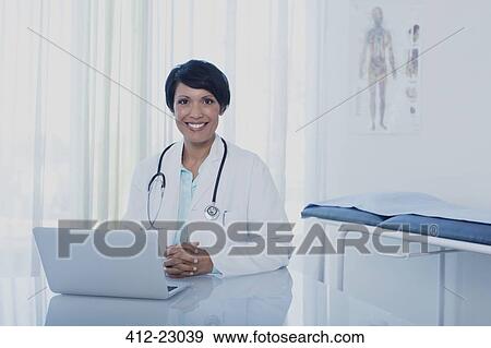 Portrait of smiling female doctor sitting at desk with laptop in office View Large Photo Image Stock Photo - Portrait of smiling female doctor sitting at desk with laptop in office. Fotosearch