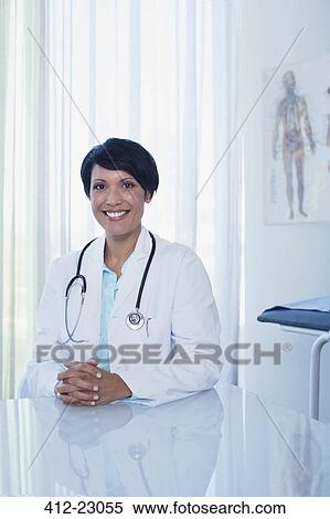 Stock Photography - Portrait of smiling female doctor sitting at desk in office. Fotosearch