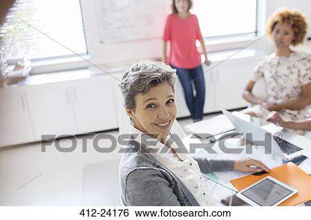 Stock Photograph - Portrait of smiling mature businesswoman at desk in office. Fotosearch