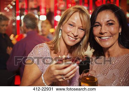 Stock Image - Portrait of smiling mature women enjoying drink in bar. Fotosearch