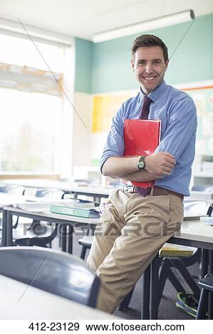 Stock Photo - Portrait of smiling teacher leaning at desk in classroom. Fotosearch