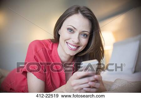 Portrait of smiling woman wearing red dress lying on bed with smartphone View Large Photo Image Stock Photo - Portrait of smiling woman wearing red dress lying on bed with smartphone . Fotosearch