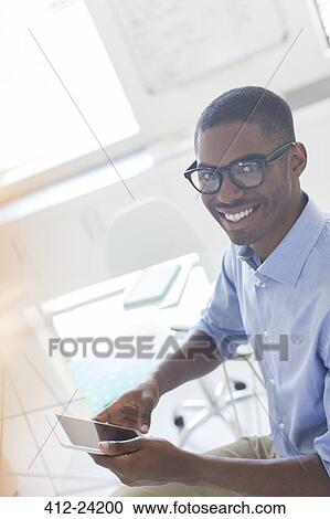 Stock Image - Portrait of smiling young businessman using smart phone in office. Fotosearch