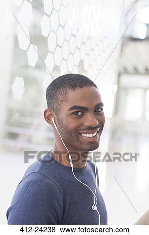 Stock Photo - Portrait of smiling young man with earphones in office. Fotosearch