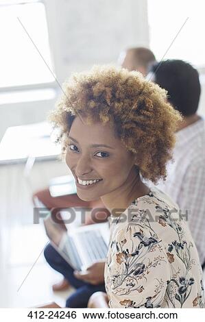 Portrait of smiling young woman in office, colleagues in background View Large Photo Image Stock Photograph - Portrait of smiling young woman in office, colleagues in background. Fotosearch