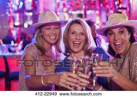 Stock Photo - Portrait of three cheerful women wearing cowboy hats toasting with champagne flutes in nightclub. Fotosearch