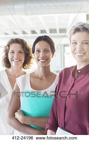 Portrait of three smiling businesswomen standing in office View Large Photo Image Stock Photograph - Portrait of three smiling businesswomen standing in office. Fotosearch