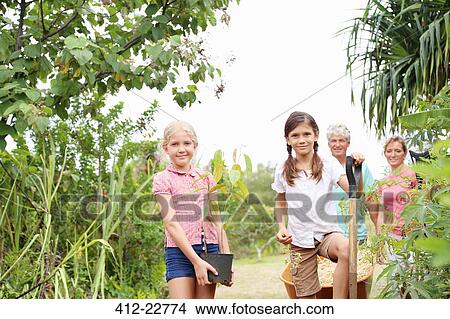 Picture - Portrait of two girls with potted plant and shovel in garden, man and woman in background. Fotosearch