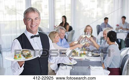 Portrait of waiter holding plate with fancy meals, people at restaurant tables in background View Large Photo Image Stock Photography - Portrait of waiter holding plate with fancy meals, people at restaurant tables in background. Fotosearch