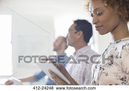 Stock Photo - Portrait of woman using tablet in office, colleagues in background. Fotosearch