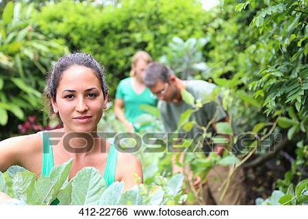 Portrait of young woman in garden, man and woman in background View Large Photo Image Stock Photograph - Portrait of young woman in garden, man and woman in background. Fotosearch