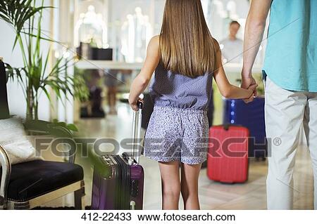 Rear view of father and daughter standing with suitcases in hotel lobby, holding hands View Large Photo Image Stock Image - Rear view of father and daughter standing with suitcases in hotel lobby, holding hands. Fotosearch