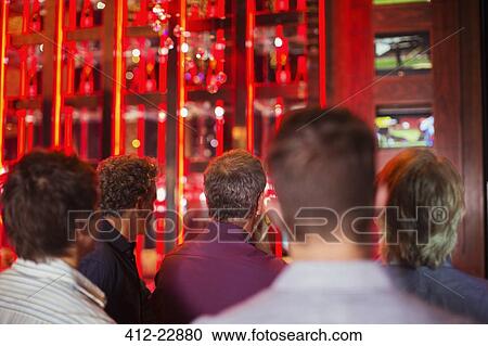 Stock Image - Rear view of group of men watching TV in bar. Fotosearch
