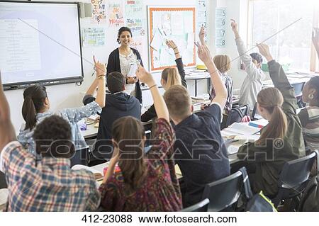 Rear view of teenage students raising hands in classroom View Large Photo Image Stock Photo - Rear view of teenage students raising hands in classroom. Fotosearch