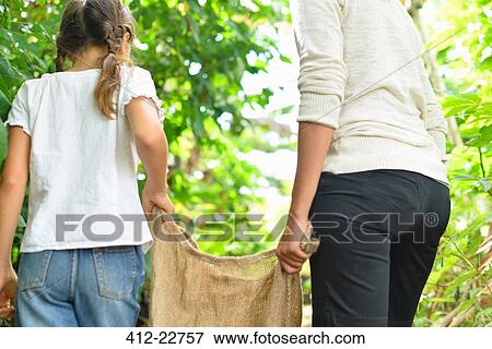 Rear view of woman and girl carrying burlap sack through garden View Large Photo Image Stock Photo - Rear view of woman and girl carrying burlap sack through garden. Fotosearch