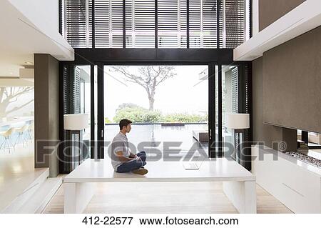 Stock Photo - Side-view of man sitting on table in front of laptop. Fotosearch