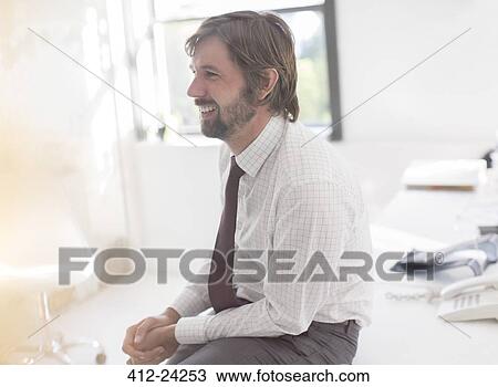 Smiling businessman wearing shirt and tie sitting on desk in office View Large Photo Image Stock Image - Smiling businessman wearing shirt and tie sitting on desk in office. Fotosearch