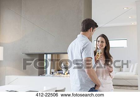 Stock Photograph - Smiling couple raising toast with champagne flutes in living room. Fotosearch