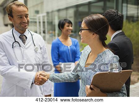 Smiling doctor shaking hand with woman in front of hospital View Large Photo Image Picture - Smiling doctor shaking hand with woman in front of hospital. Fotosearch