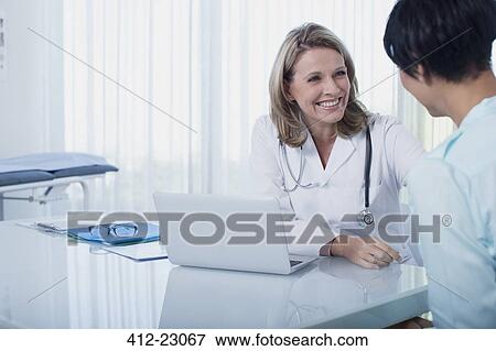 Smiling female doctor and woman sitting at desk in office View Large Photo Image Stock Photo - Smiling female doctor and woman sitting at desk in office. Fotosearch