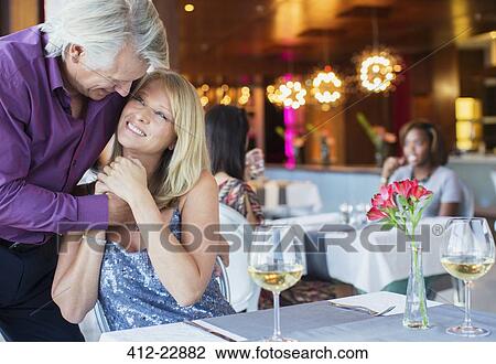 Smiling man embracing woman sitting at restaurant table with wineglasses and flowers View Large Photo Image Stock Image - Smiling man embracing woman sitting at restaurant table with wineglasses and flowers. Fotosearch