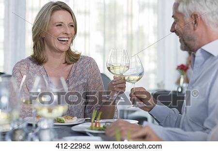 Smiling mature woman and man toasting with white wine at restaurant table View Large Photo Image Stock Image - Smiling mature woman and man toasting with white wine at restaurant table. Fotosearch