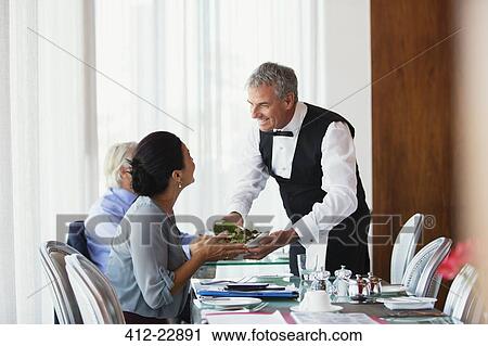 Smiling waiter serving salad to woman sitting at table in restaurant View Large Photo Image Stock Image - Smiling waiter serving salad to woman sitting at table in restaurant. Fotosearch