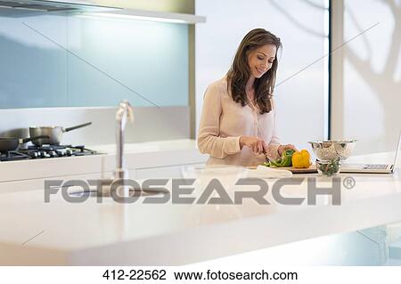 Stock Image - Smiling woman cutting bell peppers at modern kitchen counter. Fotosearch