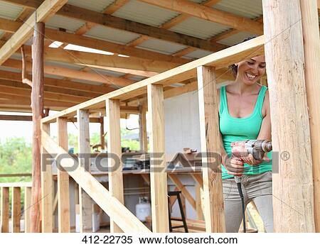 Smiling woman drilling in plank in house under construction View Large Photo Image Stock Photography - Smiling woman drilling in plank in house under construction. Fotosearch