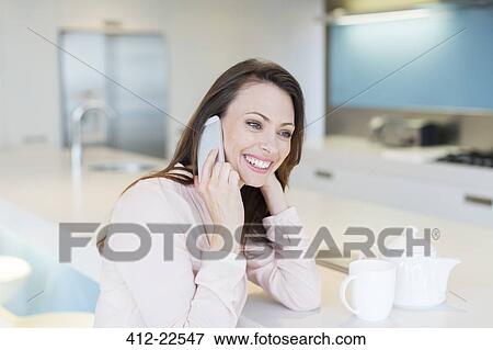 Smiling woman talking on phone in kitchen, tea cup and tea pot on counter View Large Photo Image Stock Photo - Smiling woman talking on phone in kitchen, tea cup and tea pot on counter. Fotosearch