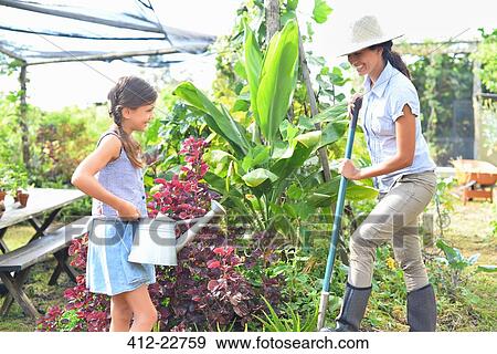 Stock Photo - Smiling woman with shovel and girl with watering can working in garden. Fotosearch