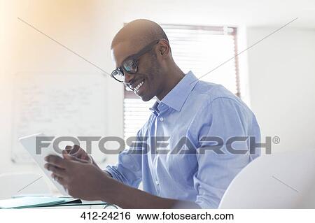 Smiling young businessman wearing glasses and blue shirt using digital tablet in office View Large Photo Image Stock Photograph - Smiling young businessman wearing glasses and blue shirt using digital tablet in office. Fotosearch