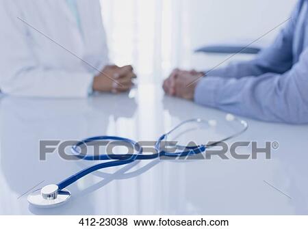 Stock Photo - Stethoscope on white desk in doctor's office, female doctor and patient sitting in background. Fotosearch