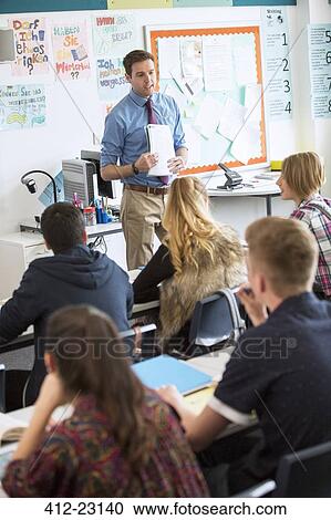 Stock Image - Teacher talking to teenage students in classroom. Fotosearch
