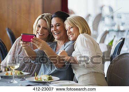 Stock Photo - Three mature women taking selfie in restaurant. Fotosearch