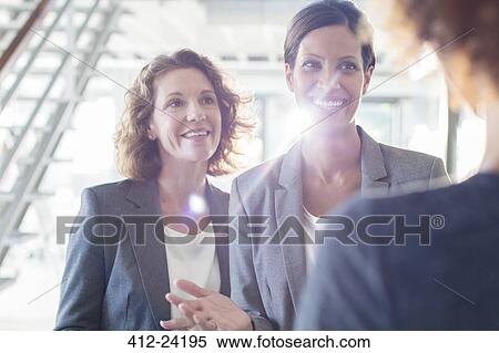 Three smiling businesswomen talking in office corridor View Large Photo Image Stock Photography - Three smiling businesswomen talking in office corridor. Fotosearch