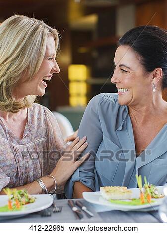 Stock Photography - Two female friends talking and laughing in restaurant, fancy dishes on table. Fotosearch