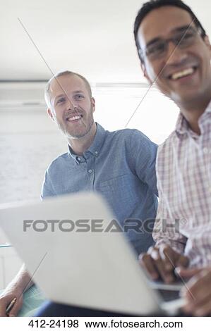 Two smiling businessmen using laptop in office View Large Photo Image Stock Photo - Two smiling businessmen using laptop in office. Fotosearch