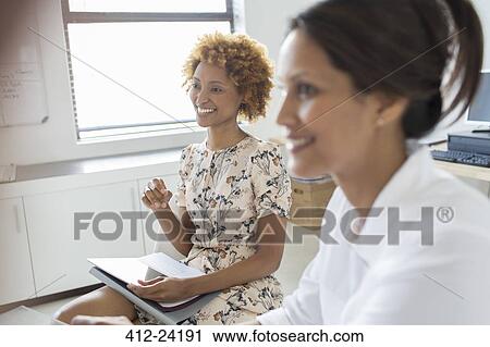 Stock Image - Two smiling businesswomen during meeting in office. Fotosearch