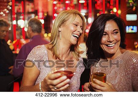 Stock Photograph - Two smiling mature women enjoying drinks in nightclub. Fotosearch