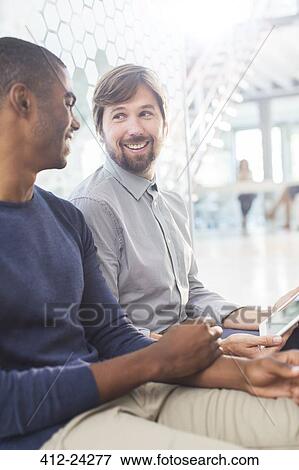 Two smiling men talking, holding digital tablet in office corridor View Large Photo Image Stock Photo - Two smiling men talking, holding digital tablet in office corridor. Fotosearch