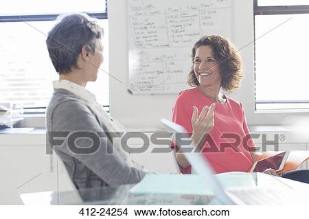 Two smiling women talking in office, whiteboard in background View Large Photo Image Picture - Two smiling women talking in office, whiteboard in background. Fotosearch