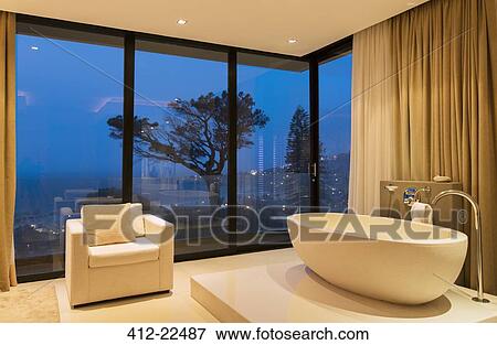 Stock Photo - View of luxurious bathroom with bathtub and armchair at night. Fotosearch