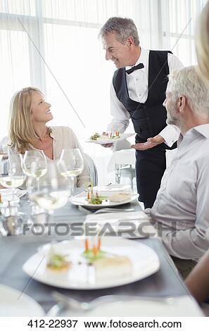 Stock Photo - Waiter serving fancy dish to woman sitting at restaurant table. Fotosearch