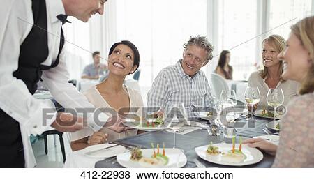 Stock Photo - Waiter serving fancy dish to woman sitting at restaurant table. Fotosearch