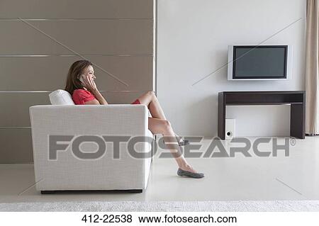 Woman in red dress sitting in armchair and talking on phone in modern living room View Large Photo Image Stock Photo - Woman in red dress sitting in armchair and talking on phone in modern living room. Fotosearch