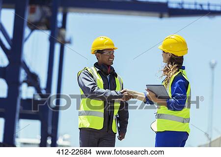Picture - Worker and businessman shaking hands near cargo crane. Fotosearch
