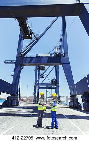 Worker and businessman talking under cargo crane at waterfront View Large Photo Image Stock Photography - Worker and businessman talking under cargo crane at waterfront. Fotosearch